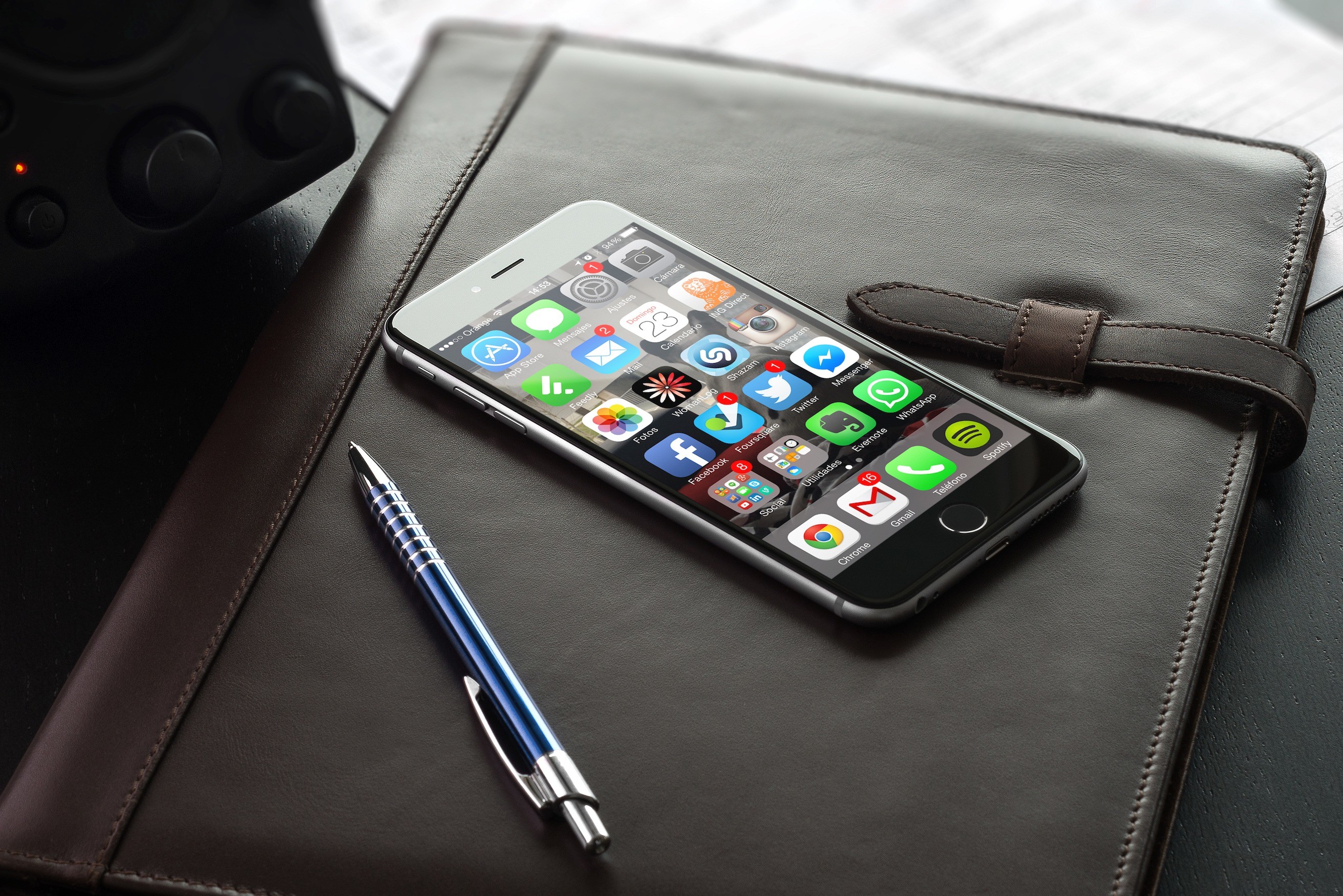 An image of an iPhone laying on a desk showing it's home screen with social media icons on it.
